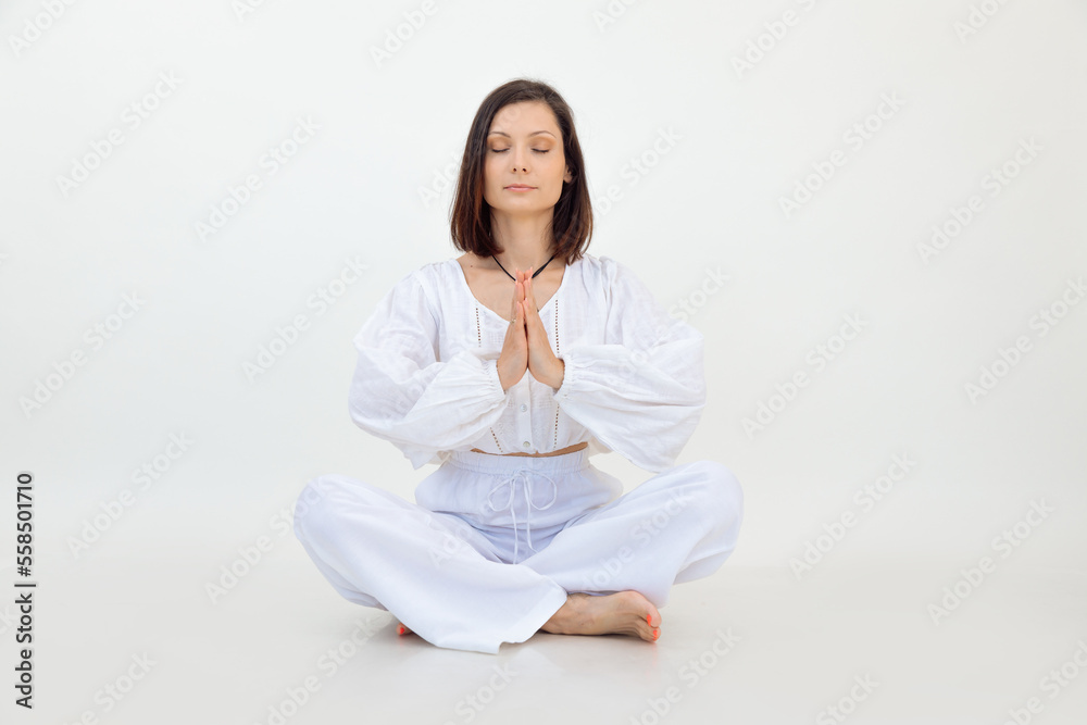 Young calm woman sitting with crossed legs on floor, folding hands with closed eyes, meditating on white background. Young calm woman sitting with crossed legs on floor, folding hands with closed eyes, meditating on white background.