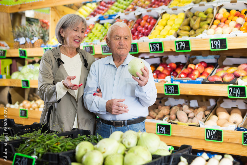 Old man and woman choosing vegetables while standing in salesroom of greengrocer.
