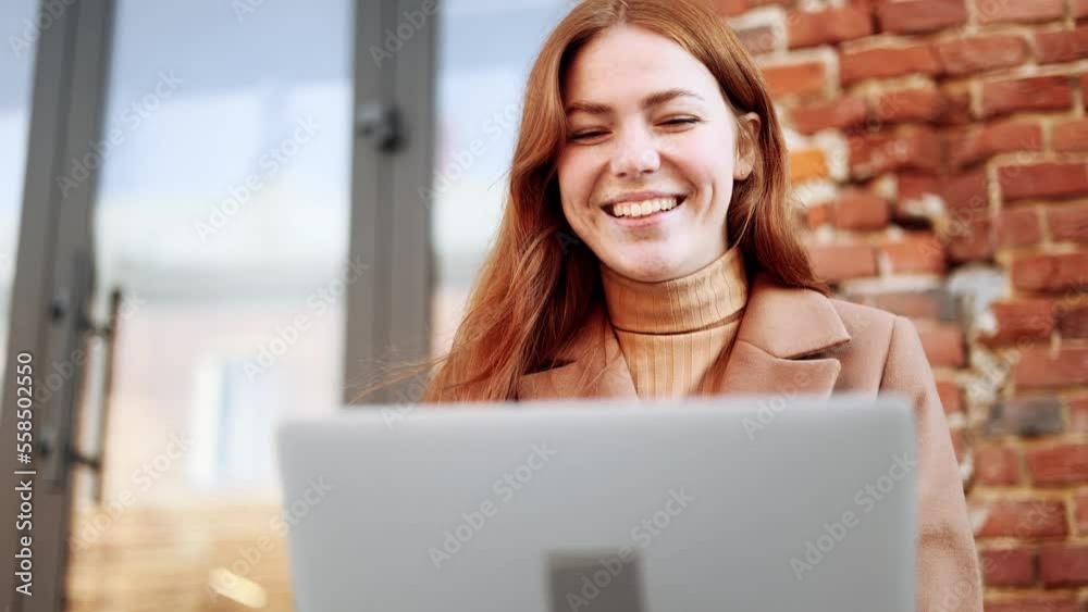 Close up portrait of young red haired ginger woman have a video call conference meeting conversation on laptop in the brick city street Happy smiling female with freckles talking by webcam outdoors Close up portrait of young red haired ginger woman have a video call conference meeting conversation on laptop in the brick city street Happy smiling female with freckles talking by webcam outdoors