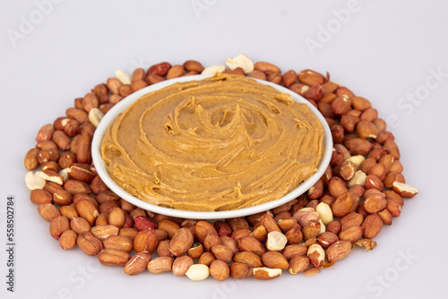 Creamy peanut butter, peanut butter in an open glass jar in the center of a peanut food background. Peanuts in shell, peeled peanuts on a white background. Vegan food concept. Creamy peanut