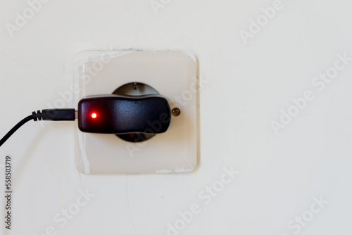 Electric plug in a white wall with a red light on it.