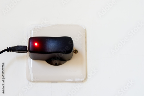 Electric plug in a white wall with a red light on it.