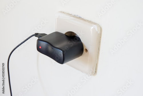 Electric plug in a white wall with a red light on it.