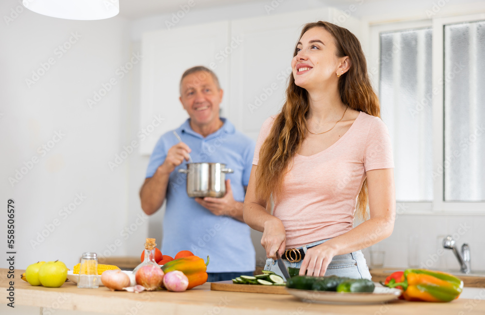 Happy elderly father and adult daughter preparing lunch together in a modern kitchen
