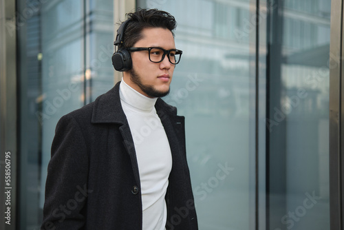 An Asian guy businessman in a headphones walks past office building.