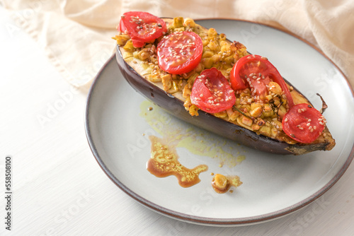 Healthy vegetarian low carb meal, baked eggplant with turmeric, ginger, onions, tomatoes and sesame seed on a plate on a white wooden table, copy space, selected focus