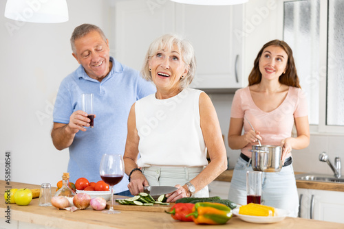 Positive senior couple spending time together with their adult daughter  cooking delicious meals for dinner