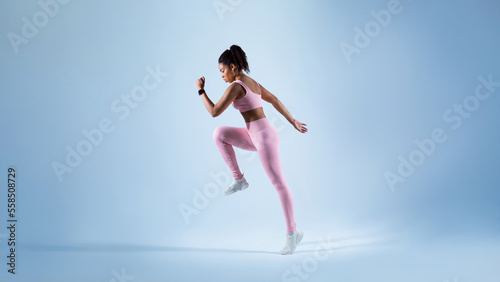 Side view of fit black lady exercising, running on blue studio background, free copy space, panorama