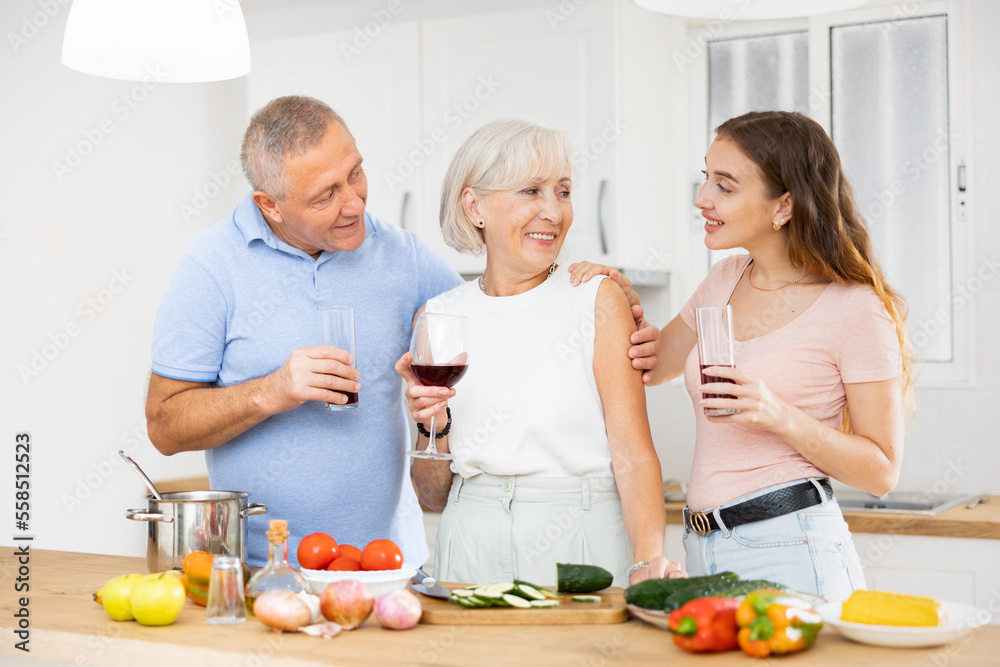 Positive senior couple spending time together with their adult daughter, cooking delicious meals for dinner
