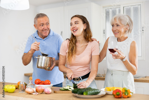 Happy smiling parents enjoy weekend cook with adult daughter in kitchen