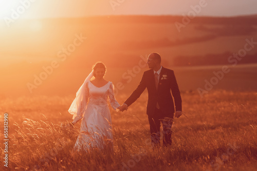 The bride and groom hold hands and look to the future in the middle of nature, the newlyweds walk together,wedding photography,until death do us part
