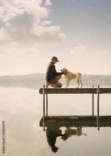 Man petting dog on the dock of a lake on a summer day.