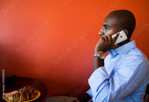 A young Ethiopian business man, talks on his cellular phone while city in a cafe with a bright red background photo