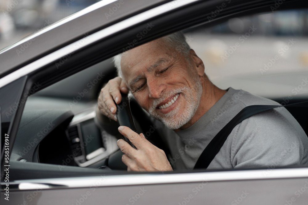 Happy senior man driver leaning his head on the steering wheel, expressing happiness, buying new car