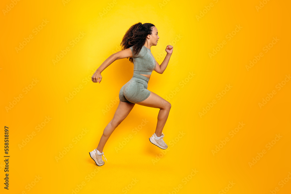 Full length side view photo of a fitness sporty brazilian or hispanic woman in sportswear, training working out, jumping, running, looking aside, isolated orange background. Sports lifestyle