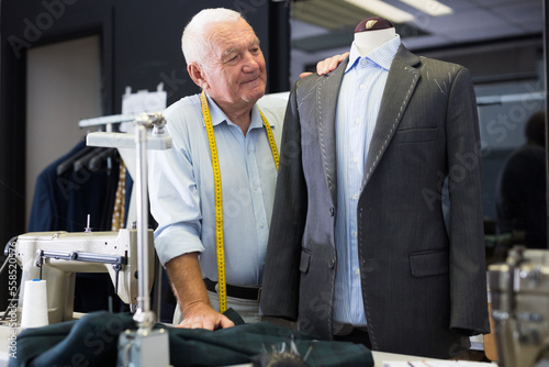 Experienced tailor tries on a new jacket on a mannequin in a workshop
