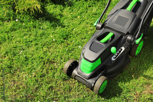 Lawn mower on green grass in garden, above view. Space for text