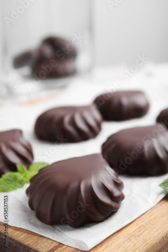 Delicious chocolate covered zephyrs and mint on wooden board, closeup. Space for text