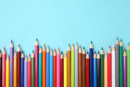 Colorful wooden pencils on light blue background, flat lay. Space for text