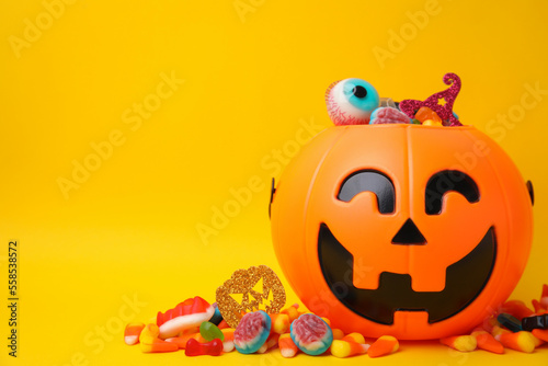 Halloween trick or treat bucket with different sweets on yellow background, space for text