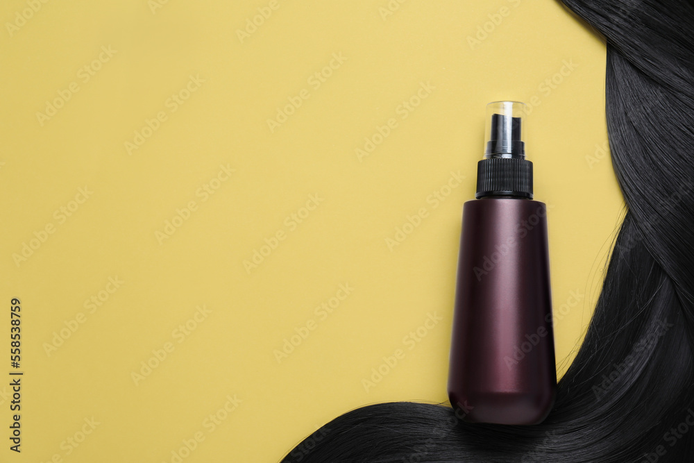 Spray bottle with thermal protection and lock of black hair on yellow background, flat lay. Space for text Spray bottle with thermal protection and lock of black hair on yellow background, flat lay. Space for text