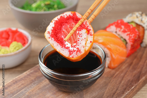 Holding delicious sushi roll with chopsticks at wooden table, closeup