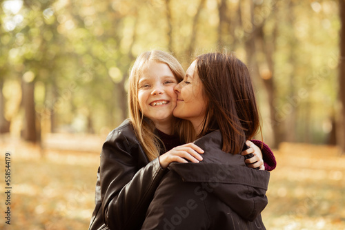 Portrait of family of young woman and teenage girl walking in forest. Mother holding daughter in arms, kissing cheek.