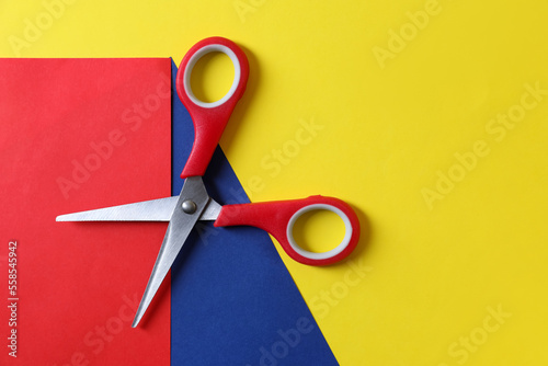 Red scissors and color sheets of paper on yellow background, top view. Space for text