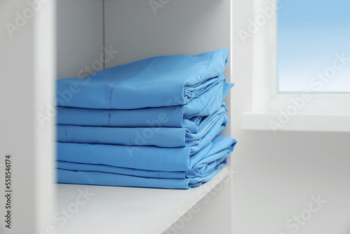 Light blue medical uniforms on white rack indoors, space for text