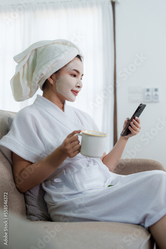 Woman with facial mask using phone at home. Skin care, face treatment, spa, cosmetology and natural beauty concept.