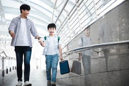 Asian father with his son walking on cityscape after shopping mall with shopping bag and bright smile. E-commerce and discounts. Big surprise mide years. Relationship and happiness.