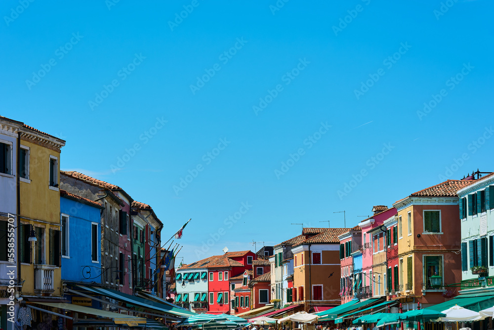 View of top part of buildings forming a line against blue cloudless sky on sunny spring day in Burano, Italy. Background with copy space.