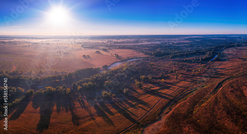 The channel and bends of the river, on a marshy meadow. Orange dry grass, scorched by the summer heat, and morning fog. A wonderful landscape at dawn. Drone view. © maykal
