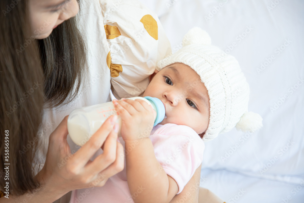 Mother feeding newborn with formula in a bottle on bed in the bedroom. Close up mother's hand hold bottle milk for feeding her daughter in house.