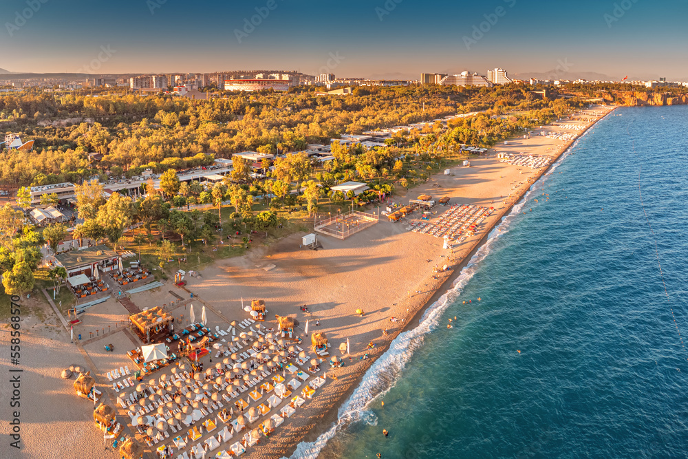 Naklejka premium Aerial view of scenic and popular Konyaalti beach in Antalya resort town. Majestic mountains with haze in the background. Vacation and holiday in Turkiye