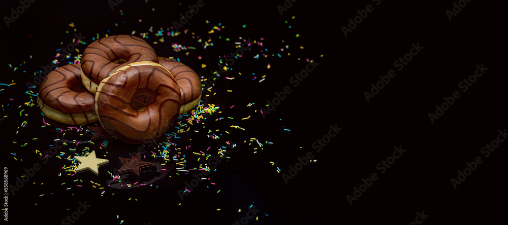 Obraz premium Donaty na tłusty czwartek. Obwarzanki na tłusty czwartek. Słodki deser do kawy. Donaty z kolorową posypką na czarnym tle. Desery do kawy, Słodkie przekąski, czekoladowy obwarzanki z posypką,