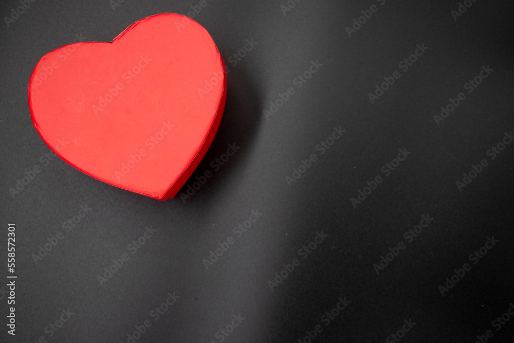 Fototapeta premium Red heart shaped gift box and dried red rose leafs on black background,Valentine's Day or birthday concept, copy space area 