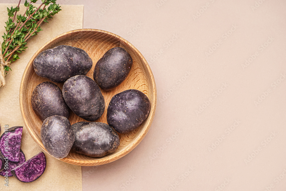 Obraz premium Wooden bowl with raw purple potatoes and thyme on color background