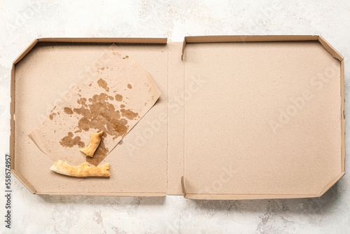 Cardboard greasy box with pizza leftovers on light background