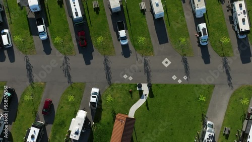 RV park aerial top down pan across mobile homes parked in grassy parking lot with resident walking down driveway
