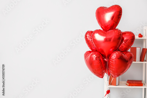 Heart-shaped balloons for Valentine's Day and bookcase near light wall