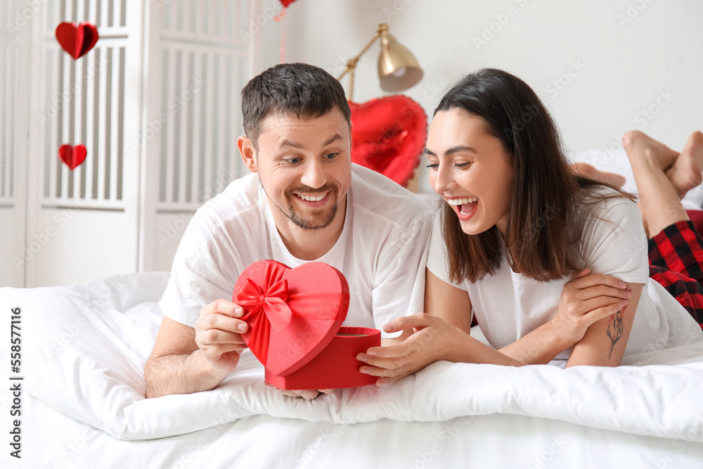 Happy couple in love opening gift in bedroom on Valentine's Day Happy couple in love opening gift in bedroom on Valentine's Day