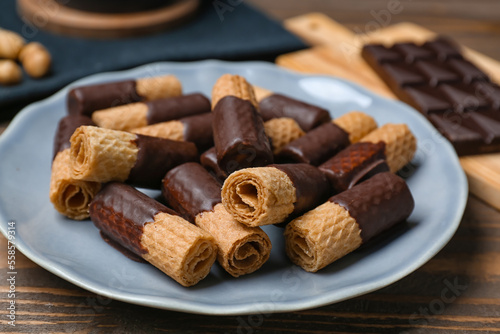Plate with tasty wafer rolls and chocolate on wooden background, closeup