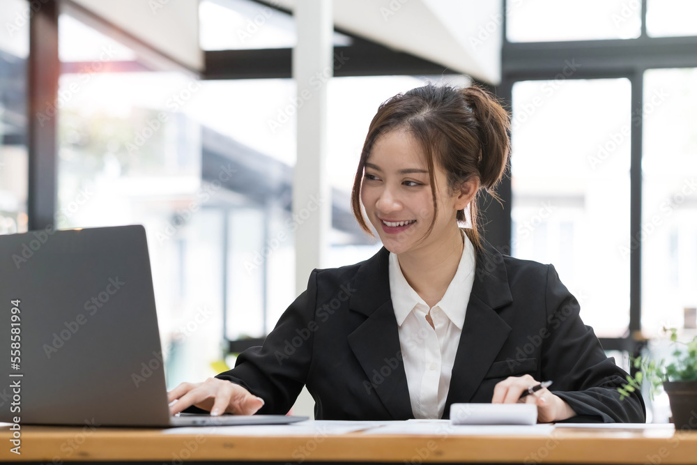 Beautiful Asian business woman using her laptop to work and enjoy working, taking note, reviewing assignment and smiling in the office. Beautiful Asian business woman using her laptop to work and enjoy working, taking note, reviewing assignment and smiling in the office.