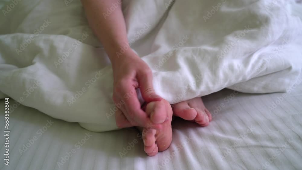 woman scratching her feet between her toes in bed, foot fungus disease woman scratching her feet between her toes in bed, foot fungus disease