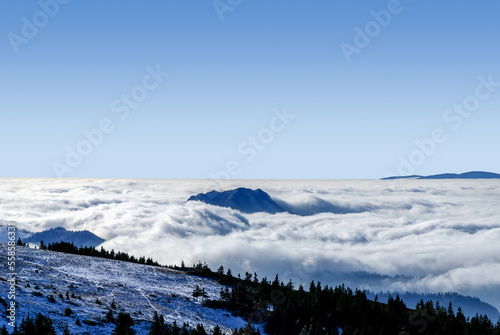 Fototapeta Naklejka Na Ścianę i Meble -  An epic ocean of clouds and fog in the winter mountains landscape, aerial view. Huge white clouds come in waves over the foggy valleys, mountain peaks rise over like islands. Dramatic overcast sky