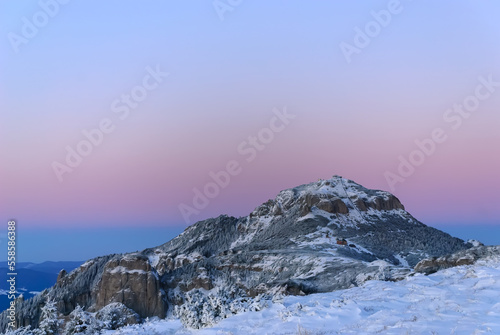 Majestic alpine scenery of mountains landscape in the evening. Sun sends its last rays over the lonely mountain peak, with slopes covered in frozen creeping pine. Beautiful blue and pink clear sky