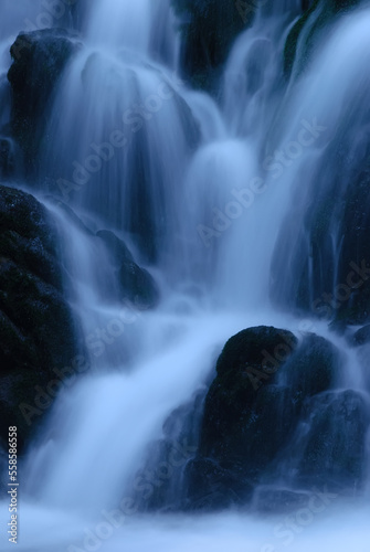 Beautiful mountain rainforest waterfall with fast flowing water and rocks  long exposure. Natural seasonal travel outdoor background with sun shining. Stream waterfall on rocks in the forest