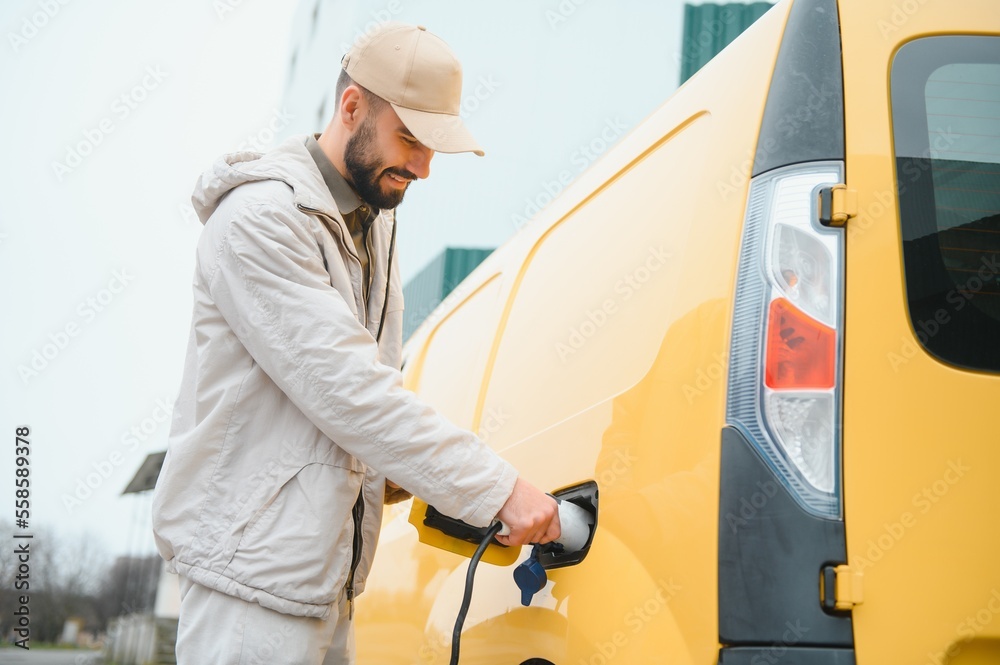 Casual man near electric car waiting for the finish of the battery charging process