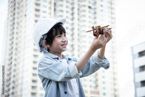 Engineer Asian boy playing wooden airplane in the park outside near cityscape. Boy running with a toy plane outdoors. Role play concept.